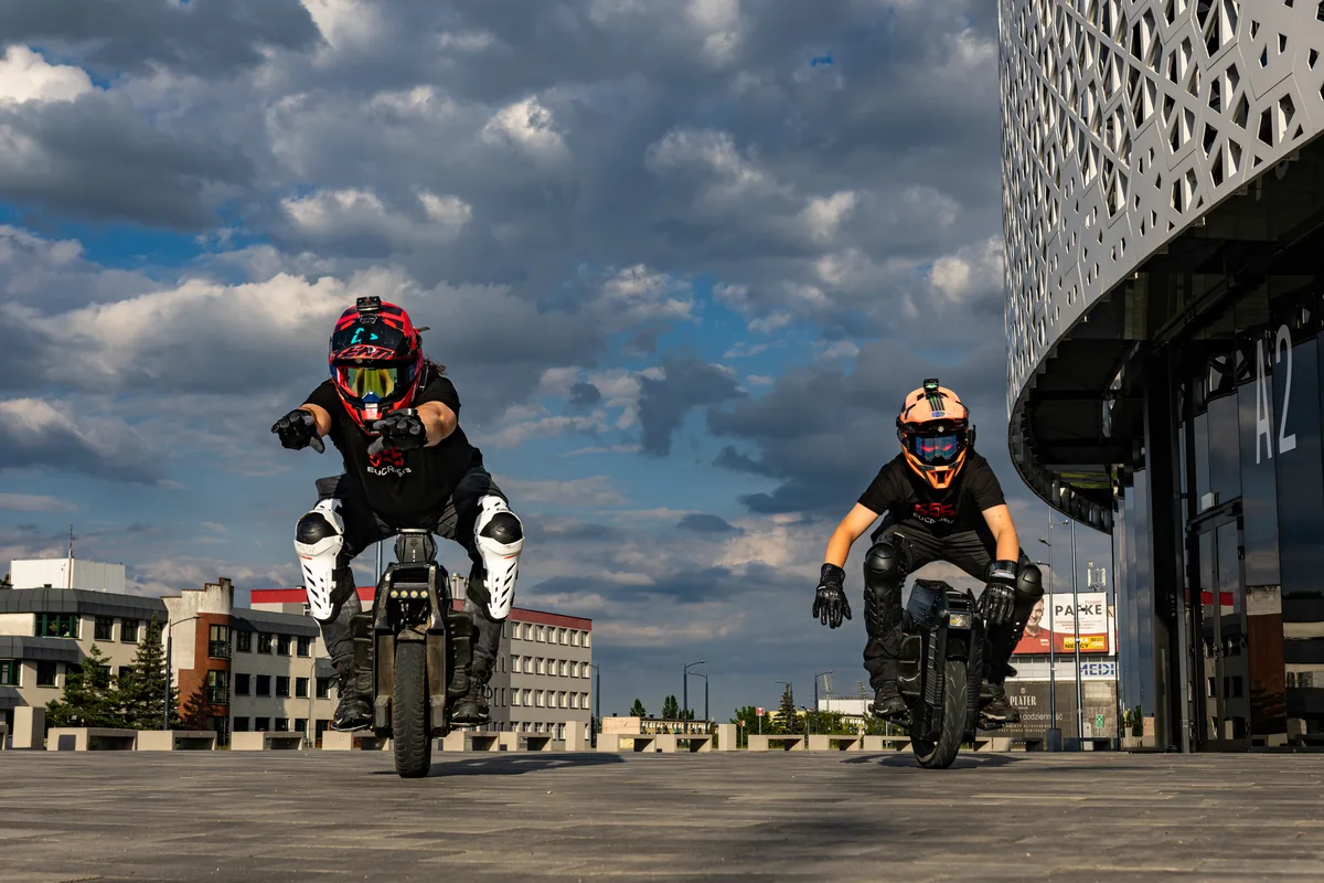 Two electric unicycle riders approaching the camera outside Urania in Olsztyn.