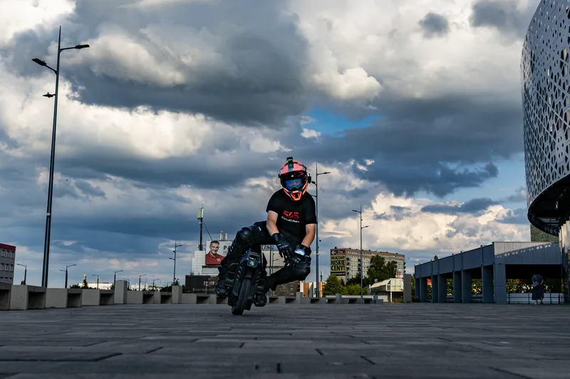 Electric unicycle rider crossing the open plaza under storm clouds in Olsztyn.